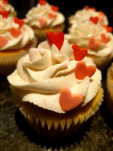 Buttercream swirls on top of  a cupcake with 4 different colour hearts on.