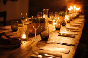 A wood table set with wine glasses with a warm light from the candles on the table. 