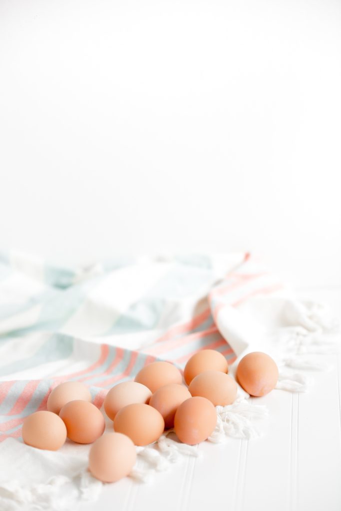 12 light brown eggs laid on a soft, striped kitchen towel.